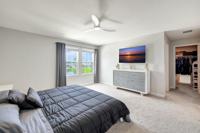 bedroom with baseboards, light colored carpet, a textured ceiling, and visible vents