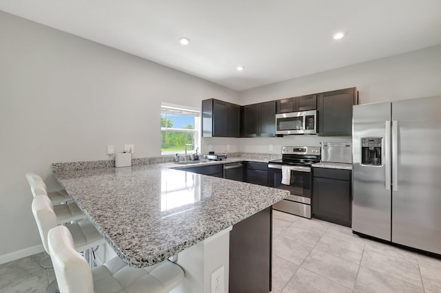 kitchen featuring stainless steel appliances, a peninsula, light stone counters, a kitchen breakfast bar, and a sink