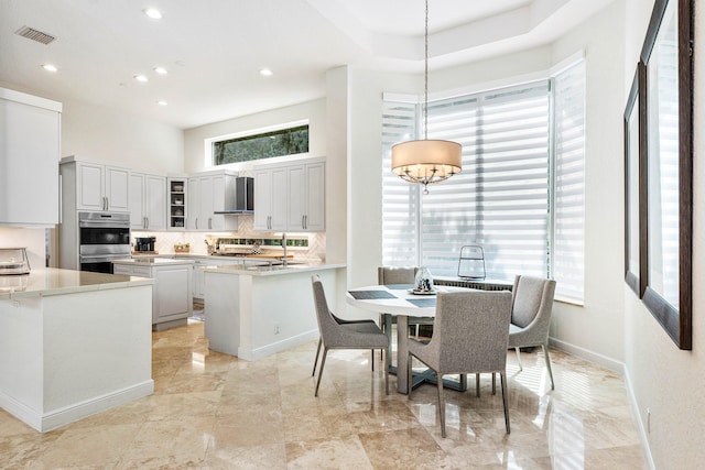 kitchen with wall chimney range hood, double oven, plenty of natural light, and hanging light fixtures