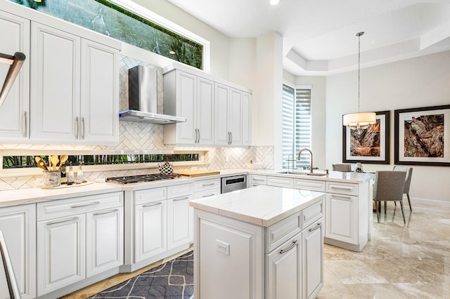 kitchen with wall chimney range hood, hanging light fixtures, sink, stainless steel gas cooktop, and a center island