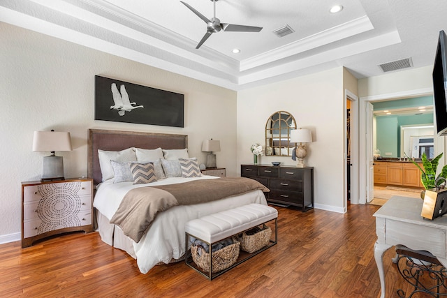 bedroom featuring a raised ceiling, ceiling fan, ornamental molding, dark hardwood / wood-style floors, and ensuite bathroom