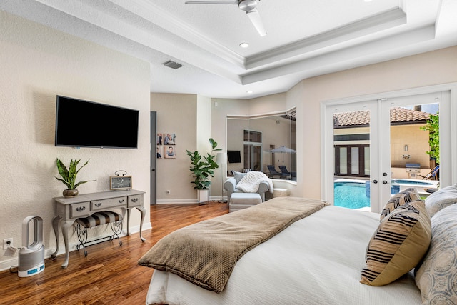 bedroom featuring french doors, access to exterior, a tray ceiling, hardwood / wood-style floors, and ceiling fan