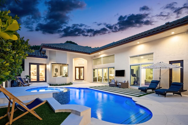 pool at dusk with an in ground hot tub, a patio, and french doors