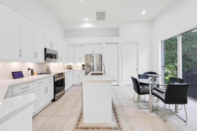 kitchen with white cabinets, appliances with stainless steel finishes, sink, light tile patterned flooring, and a kitchen island with sink