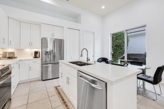 kitchen with an island with sink, stainless steel appliances, sink, white cabinets, and light tile patterned flooring