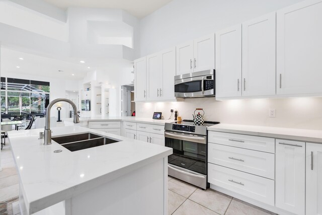 kitchen with light tile patterned floors, light stone counters, sink, appliances with stainless steel finishes, and white cabinets