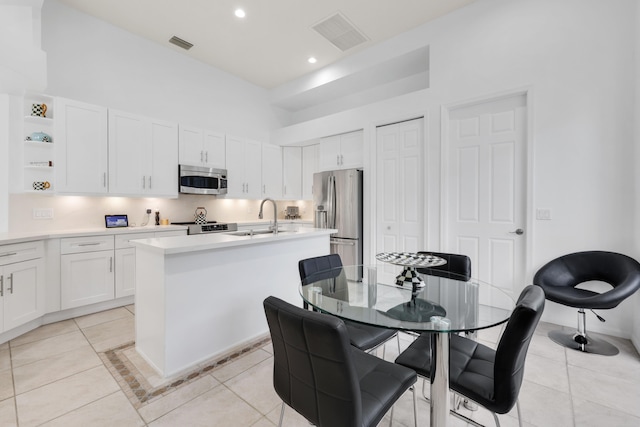 kitchen with white cabinets, stainless steel appliances, sink, an island with sink, and light tile patterned flooring