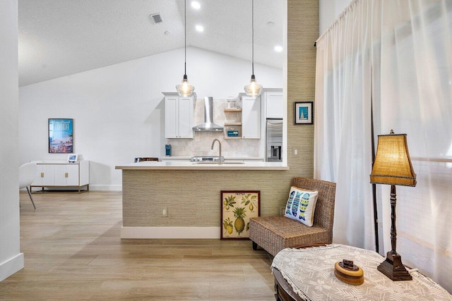 kitchen featuring wall chimney range hood, stainless steel fridge with ice dispenser, light hardwood / wood-style floors, white cabinetry, and hanging light fixtures