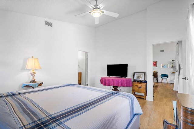 bedroom with ceiling fan, light wood-type flooring, a textured ceiling, and a towering ceiling