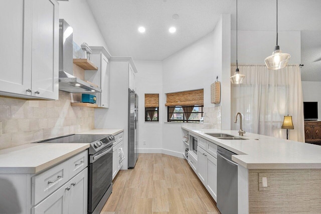 kitchen with sink, wall chimney exhaust hood, stainless steel appliances, decorative light fixtures, and white cabinets