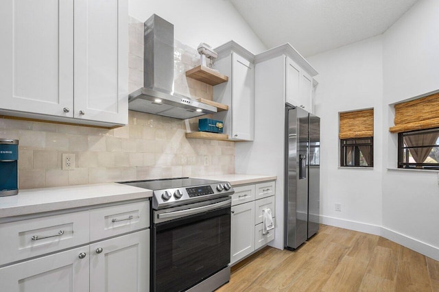 kitchen with lofted ceiling, wall chimney range hood, light hardwood / wood-style floors, white cabinetry, and stainless steel appliances