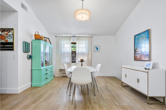 dining area with lofted ceiling, a textured ceiling, and light hardwood / wood-style flooring