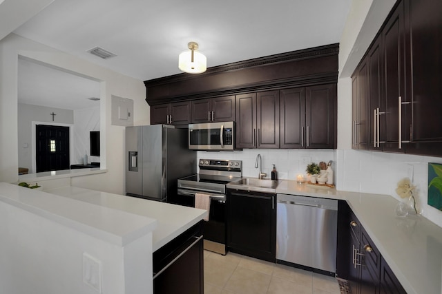 kitchen featuring dark brown cabinetry, sink, tasteful backsplash, light tile patterned floors, and appliances with stainless steel finishes