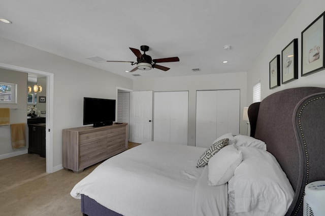 bedroom featuring ceiling fan with notable chandelier, ensuite bathroom, and multiple closets