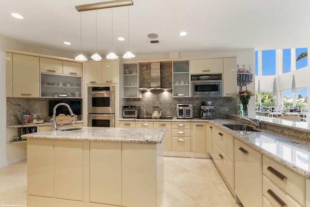 kitchen featuring stainless steel appliances, cream cabinetry, wall chimney exhaust hood, and backsplash