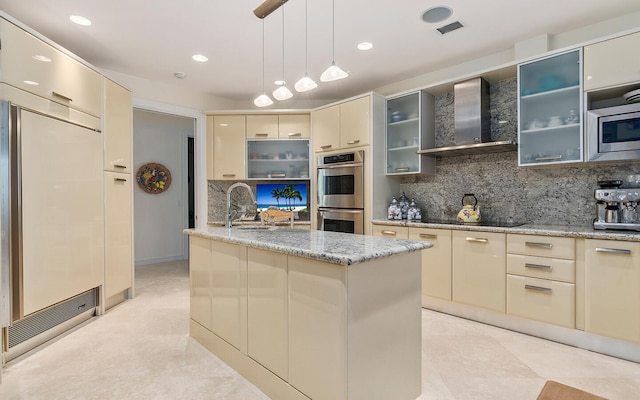 kitchen featuring cream cabinets, wall chimney range hood, appliances with stainless steel finishes, light tile patterned floors, and backsplash