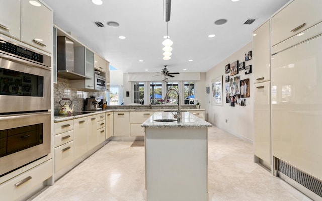 kitchen with ceiling fan, wall chimney exhaust hood, stainless steel double oven, decorative backsplash, and built in refrigerator