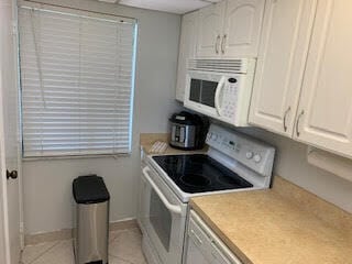 kitchen featuring white cabinetry, light tile patterned flooring, and white appliances