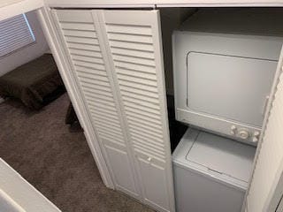 washroom with stacked washing maching and dryer and dark carpet