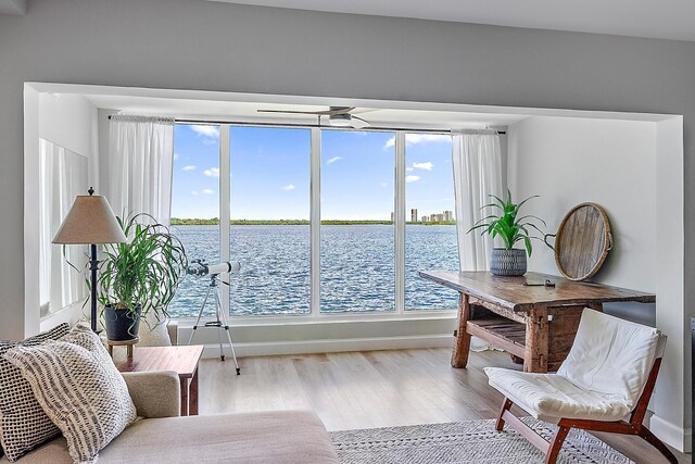 living area featuring ceiling fan, light hardwood / wood-style flooring, and a water view