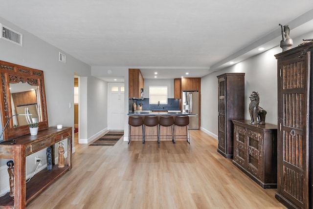 kitchen with light hardwood / wood-style flooring, a breakfast bar, stainless steel refrigerator with ice dispenser, and sink