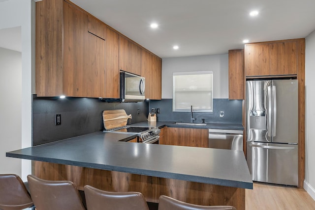 kitchen featuring tasteful backsplash, stainless steel appliances, a breakfast bar, sink, and kitchen peninsula