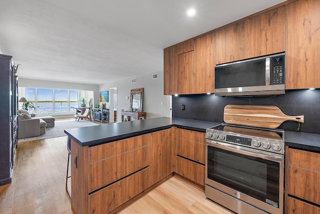 kitchen with light wood-type flooring, stainless steel appliances, and kitchen peninsula