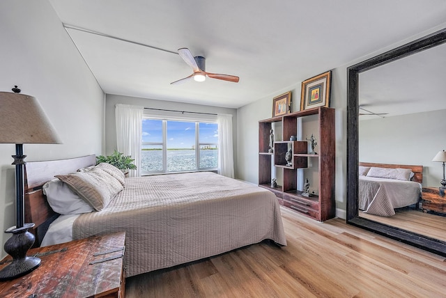 bedroom featuring a water view, light hardwood / wood-style floors, and ceiling fan