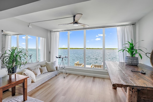 sunroom with ceiling fan and a water view