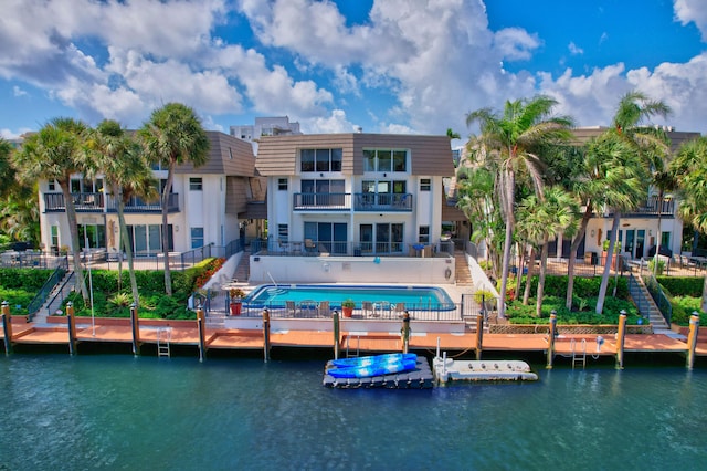 back of house featuring a balcony, a water view, and a community pool