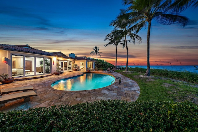 pool at dusk with an outdoor pool and a patio