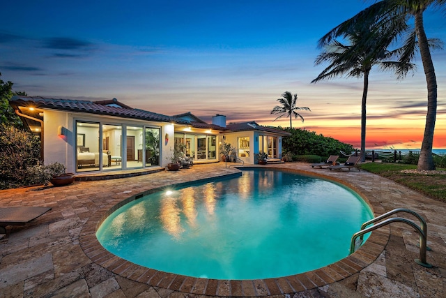 pool at dusk with a patio area and an outdoor pool