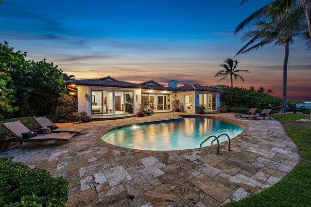 pool at dusk with french doors and a patio area