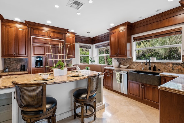 kitchen with light stone countertops, stainless steel dishwasher, pendant lighting, a breakfast bar, and sink