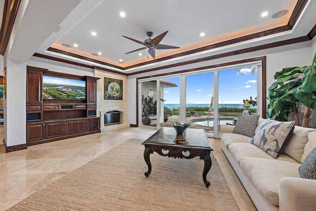 living room featuring a high end fireplace, ceiling fan, a tray ceiling, and crown molding