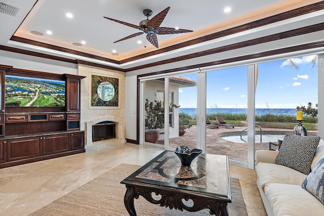 living room featuring ceiling fan, a premium fireplace, a water view, and crown molding