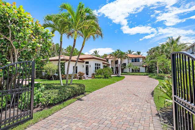 mediterranean / spanish-style house featuring a tile roof, a gate, fence, and decorative driveway