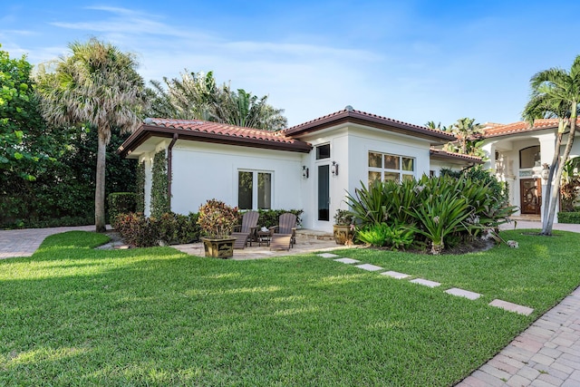 rear view of property with a yard, a patio area, a tiled roof, and stucco siding