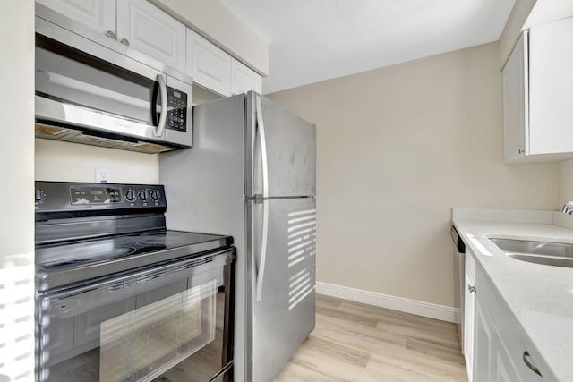 kitchen with light stone counters, white cabinets, sink, light hardwood / wood-style flooring, and appliances with stainless steel finishes