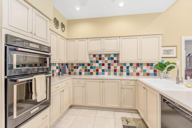 kitchen with double wall oven, stainless steel dishwasher, sink, light tile patterned floors, and cream cabinets