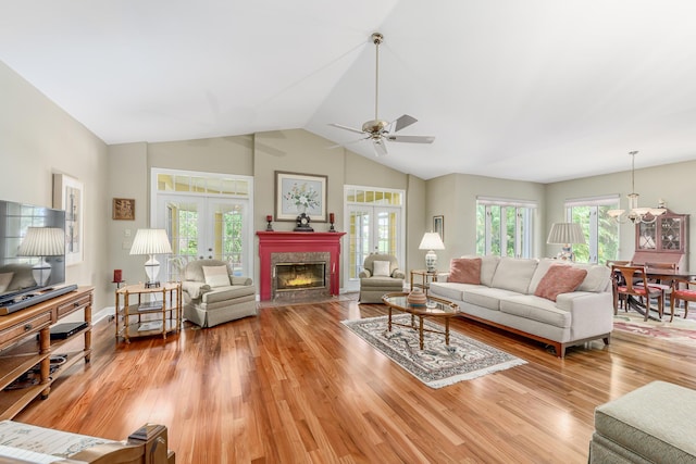 living room with ceiling fan with notable chandelier, hardwood / wood-style floors, french doors, a fireplace, and vaulted ceiling