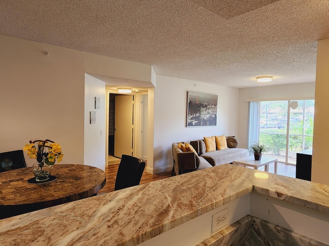 living area featuring a textured ceiling, baseboards, and wood finished floors