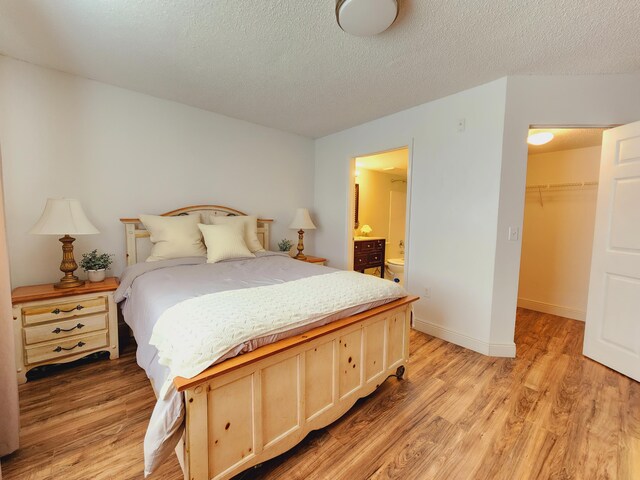 bedroom with a textured ceiling, light hardwood / wood-style flooring, a walk in closet, and a closet