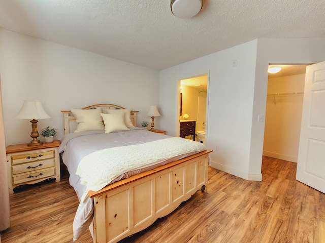 bedroom featuring a textured ceiling, baseboards, a closet, light wood-type flooring, and a walk in closet