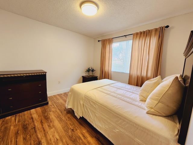 bedroom with a textured ceiling, baseboards, and wood finished floors