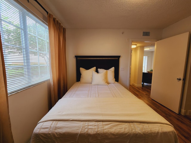 bedroom with a textured ceiling, visible vents, and wood finished floors