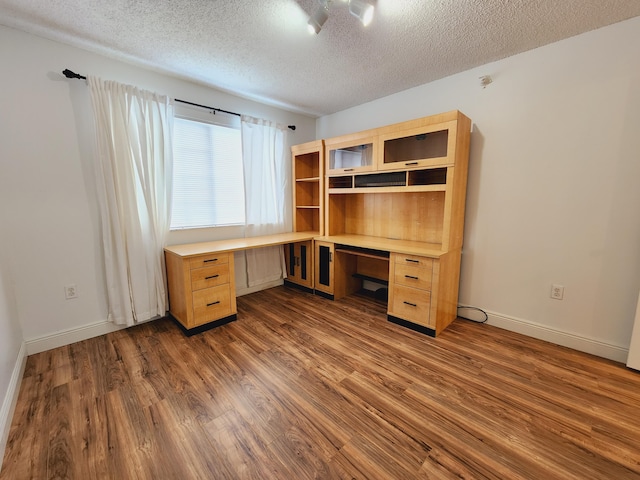 unfurnished office with a textured ceiling, baseboards, dark wood-style flooring, and built in study area