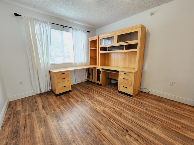 unfurnished office with dark wood-style floors, a textured ceiling, built in study area, and baseboards