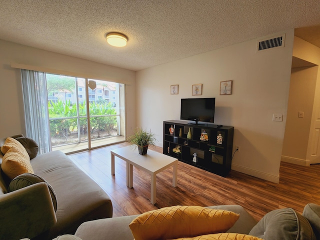 living area featuring visible vents, a textured ceiling, baseboards, and wood finished floors