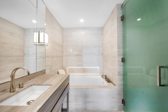 bathroom with vanity, shower with separate bathtub, and tile walls